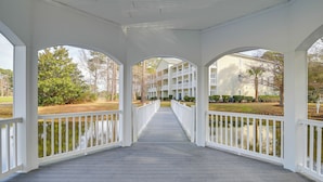 A covered wooden deck with white railings, leading to a building with multiple balconies. - Golfer’s Paradise w/ Pool! 6 Mi to Myrtle Beach (Myrtle Beach)