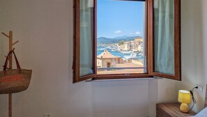 A room with a wooden-framed window, a wooden nightstand with a lamp, and a coat rack with a bag. - Porta A Mare Home Apartment with Air Conditioning (Portoferraio)