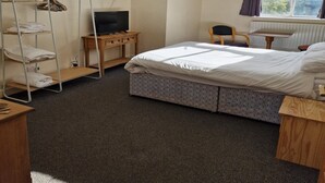 Ein kleiner, ordentlicher Raum mit einem Einzelbett, einem Fernseher auf einem Holztisch, einem Stuhl und einer Heizung.