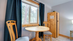 Ein Zimmer mit Holztisch und -stühlen, einem Fenster mit Vorhängen sowie einem Holzschrank.