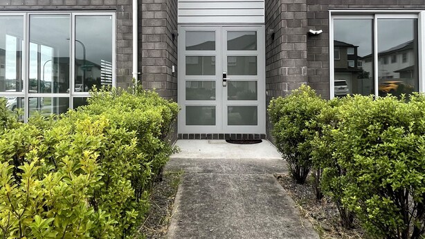 A modern building with a grey brick facade, large windows, and a central entrance with a glass door. - Parkside Elegance on Puoro St Near Shopping Centre (Auckland)