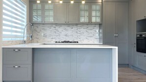 A modern kitchen with grey cabinets, a marble backsplash, and a central island. - Parkside Elegance on Puoro St Near Shopping Centre (Auckland)