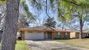 A single-story brick house with a garage, surrounded by trees and a well-maintained lawn. - 11 Mi to Dtwn Dallas: Charming Home w/ Deck & Yard (Irving)