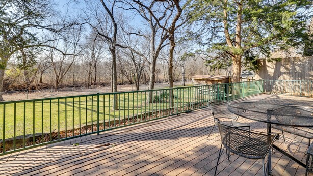 A wooden deck with a metal table and chairs, surrounded by a green metal fence and trees. - 11 Mi to Dtwn Dallas: Charming Home w/ Deck & Yard (Irving)