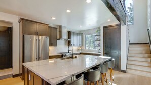Une cuisine moderne dotée d’un grand îlot central, d’appareils électroménagers en acier inoxydable et offrant une vue sur l’extérieur.