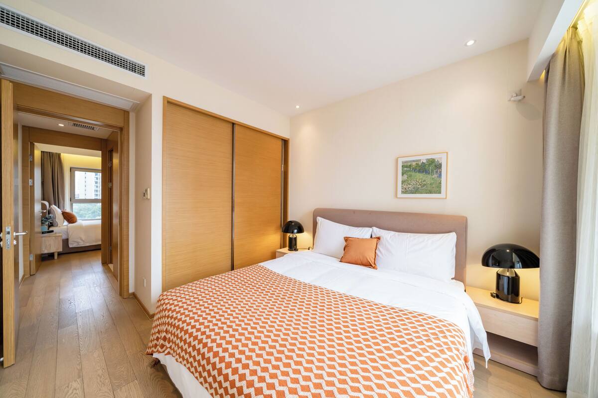 A hotel room with a large bed, a bedside table with a lamp, a wardrobe, and a view of the outdoors.