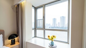 A hotel room with a large window, a bedside table with a lamp, a vase with flowers, and a book titled "STYLE". - Tyms Gubei 3BR Family Apt at Mingdu City (Shanghai)