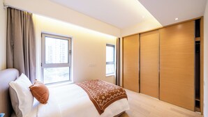 A modern hotel room with a large bed, a wooden wardrobe, and a window providing natural light. - Tyms Gubei 3BR Family Apt at Mingdu City (Shanghai)