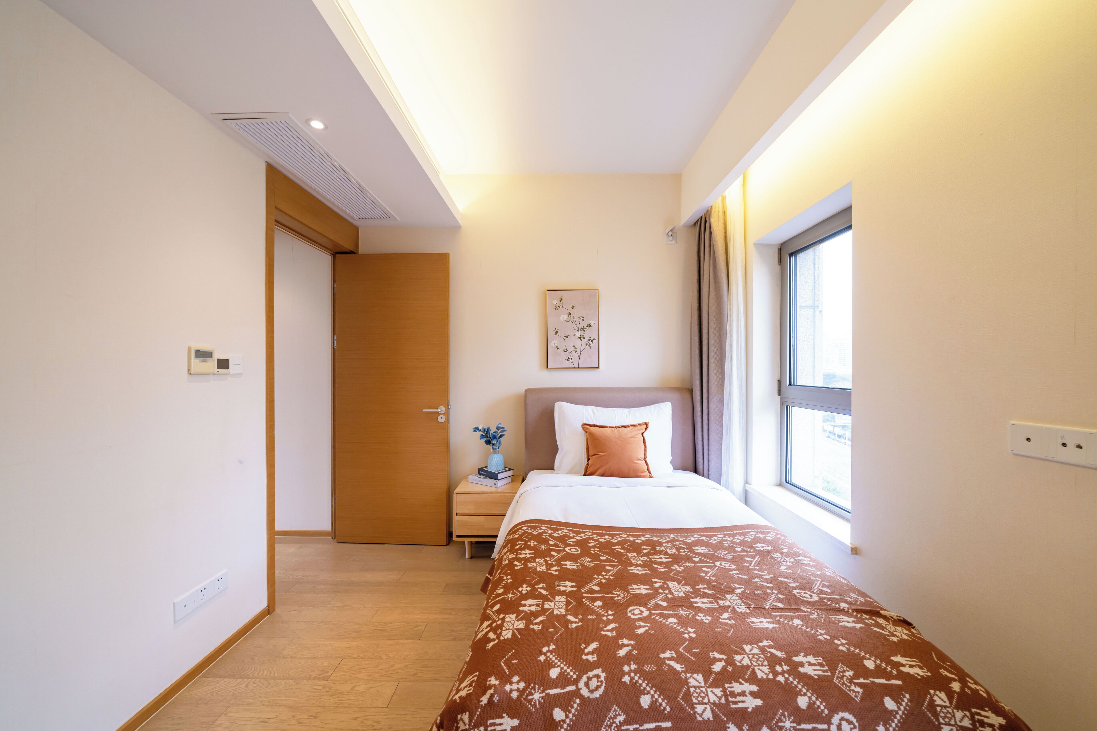 A hotel room with a bed, a nightstand, a window, and a door.
