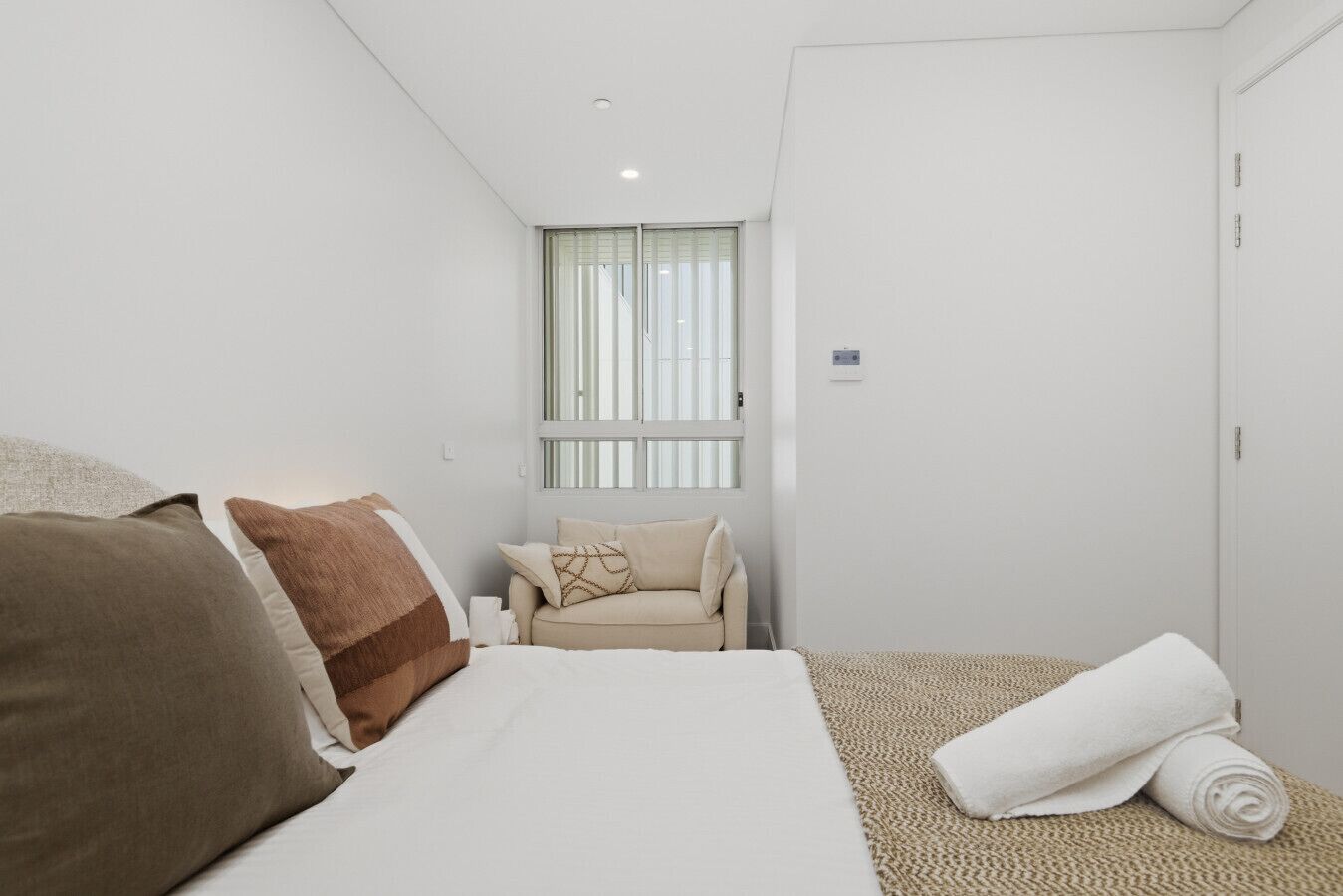 Une chambre d’hôtel minimaliste comprenant un lit, un canapé, une fenêtre et une porte.