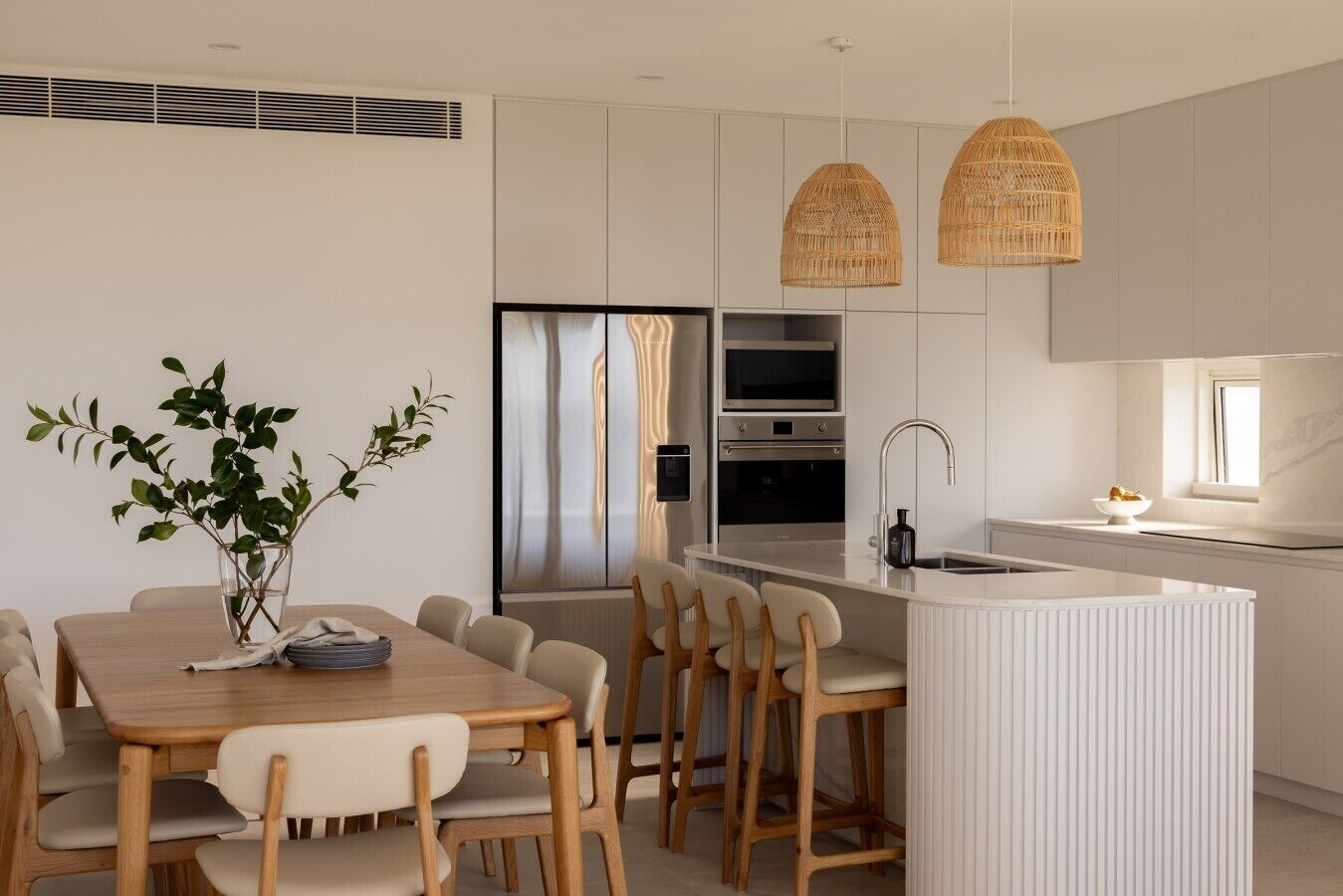 Una cocina moderna con armarios blancos, una isla central y una zona de comedor con mesa y sillas de madera.