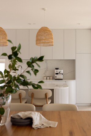 A modern kitchen with white cabinetry, a built-in coffee machine, and two wicker pendant lights. - Kailani 301: Designer Waterfront Apartment (Batemans Bay)