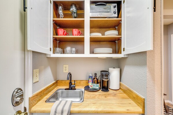 A compact kitchen with a built-in sink, wooden countertop, and open cabinets containing dishes, glasses, and a toaster. - White Mountains Adventure Base: Hike, Ski, Golf! (Pinetop-Lakeside)