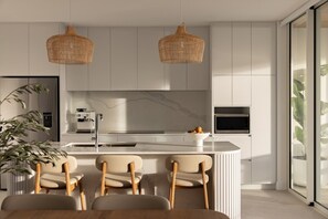 A modern kitchen with a marble backsplash, white cabinetry, a central island with bar stools, and a large window. - Kailani 202: Uninterrupted Bay & Marina Views (Batemans Bay)