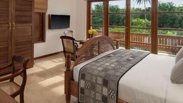 A bedroom with a bed, a wooden chair, a television, and a window with a view of greenery. - TAAVETTI (Galle)