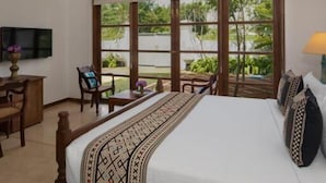 A hotel room with a large bed, a desk, a chair, a TV, and a window with a view of greenery. - TAAVETTI (Galle)