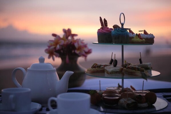 A table set with a teapot, cups, a tiered dessert stand with cupcakes and sandwiches, and a vase of flowers. - TAAVETTI (Galle)