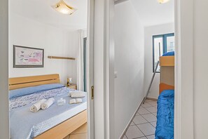 Une chambre à coucher avec un lit, une table de chevet, un tableau encadré et une porte donnant sur une autre pièce.