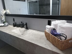 A bathroom with a large mirror, a sink, and a basket containing towels and a hairdryer. - Zermatt del Valle (Valle de Guadalupe)