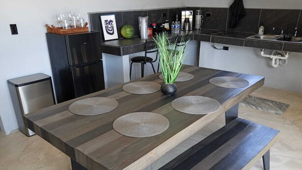 Une cuisine moderne avec une longue table à manger, des meubles de rangement noirs et un réfrigérateur noir.