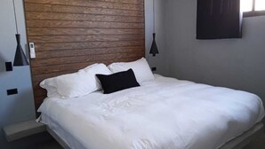 Un lit avec une literie blanche, une tête de lit en bois et deux appliques murales noires.