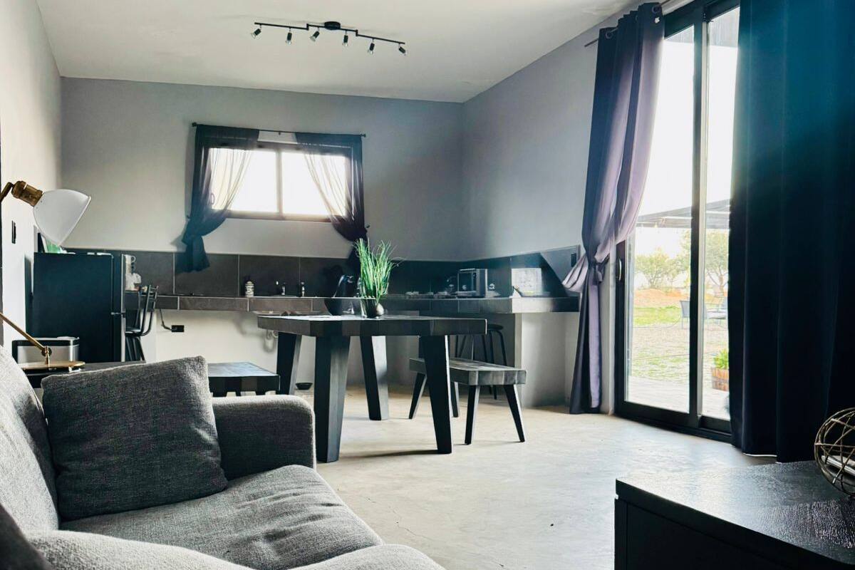 A modern living room with a grey sofa, a dining table, and a kitchen area with a window.