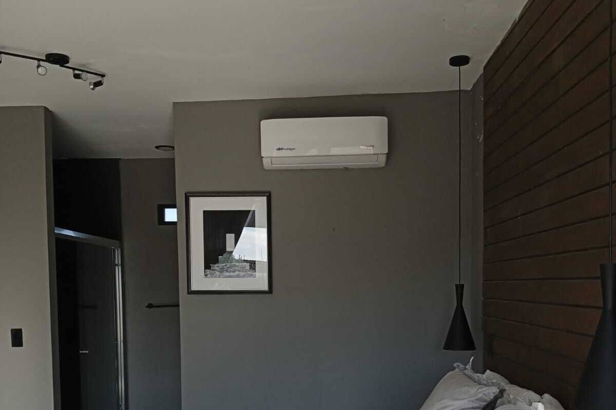 A bedroom with a bed, a wall-mounted air conditioner, a framed picture, and a pendant light.