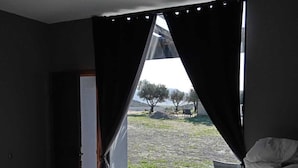 Une pièce avec un lit, une fenêtre avec des rideaux et une vue sur un espace verdoyant, avec des arbres et un bâtiment au loin.