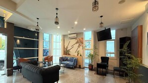 A spacious lobby with a black sofa, a blue armchair, and a dining table. There are potted plants and a large window providing natural light. - Madina inn Hotel & Hostel Yogyakarta (Yogyakarta)