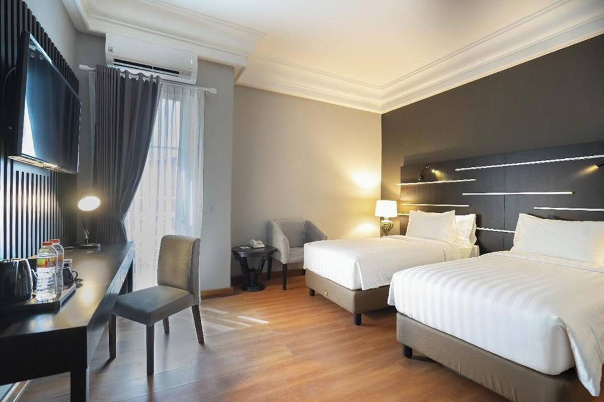 A hotel room with two beds, a desk with a chair, a TV, and a minibar.
