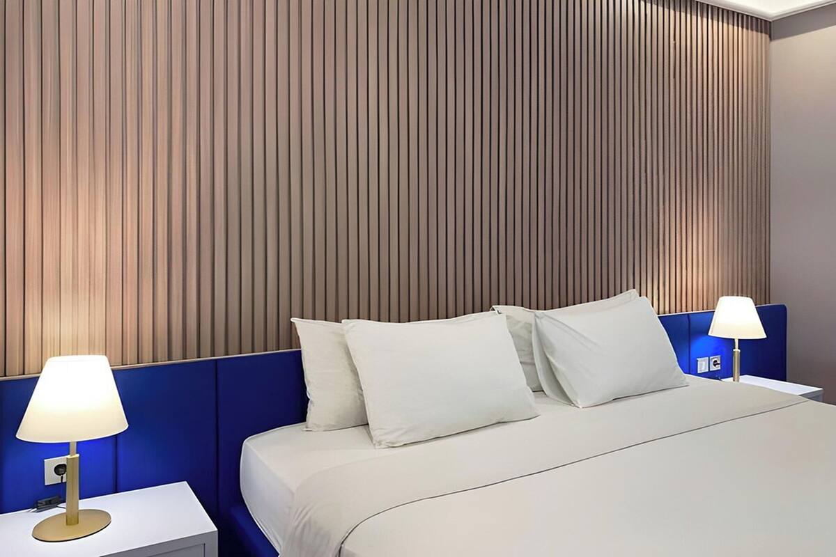 A hotel room with a bed, two bedside tables, and a wall with vertical wooden slats.