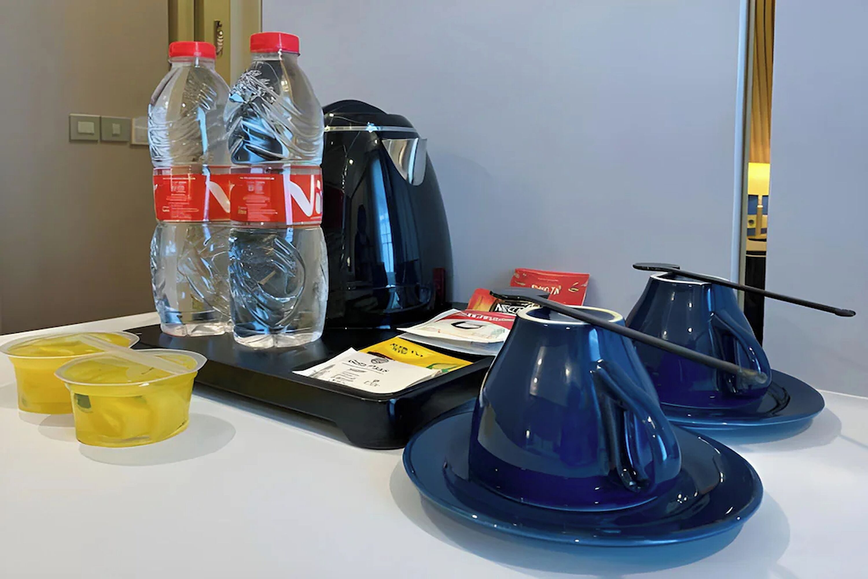 Une chambre d’hôtel équipée d’une machine à café, de deux bouteilles d’eau, de deux tasses jaunes et de deux théières bleues posées sur le comptoir.