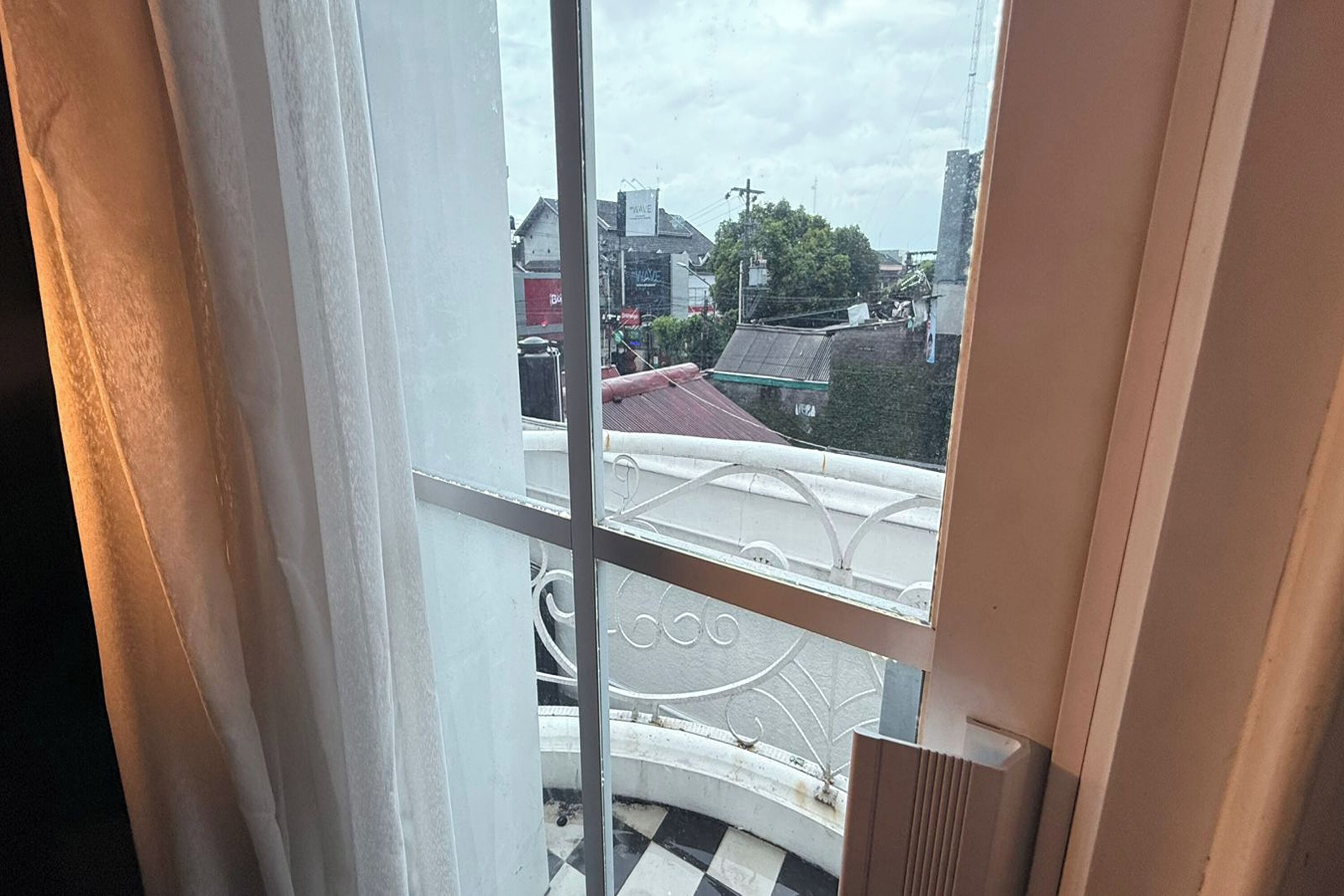 A view from a window with a metal railing, overlooking a street with buildings and a tree.