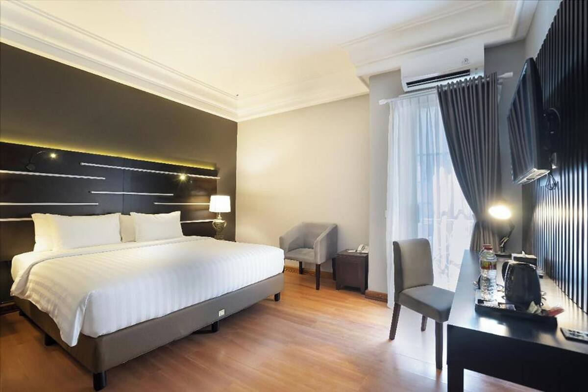 A hotel room with a large bed, a desk, a chair, and a window with curtains.