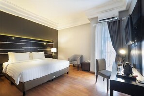 Ein Hotelzimmer mit einem großen Bett, einem Schreibtisch, einem Stuhl und einem fenster mit Vorhängen.