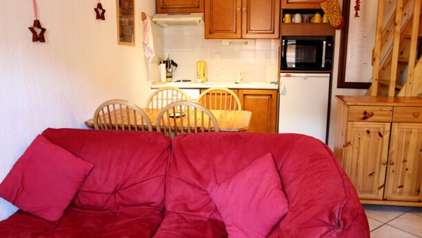 A red sofa with cushions in a kitchen area with wooden cabinets, a microwave, and a refrigerator. - Duplex in Les Carroz (Araches-la-Frasse)