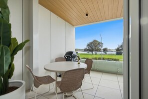 A balcony with a round table and wicker chairs, a helmet, and a bottle of wine. - Kailani 102: Luxury 3 Bed Waterfront Apartment (Batemans Bay)