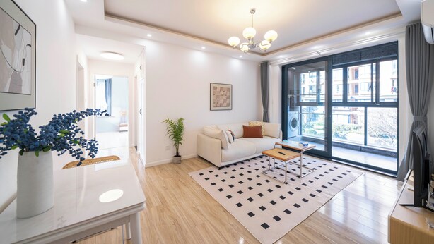 A modern living room with a sofa, a coffee table, a rug, and a large window with a view of buildings.