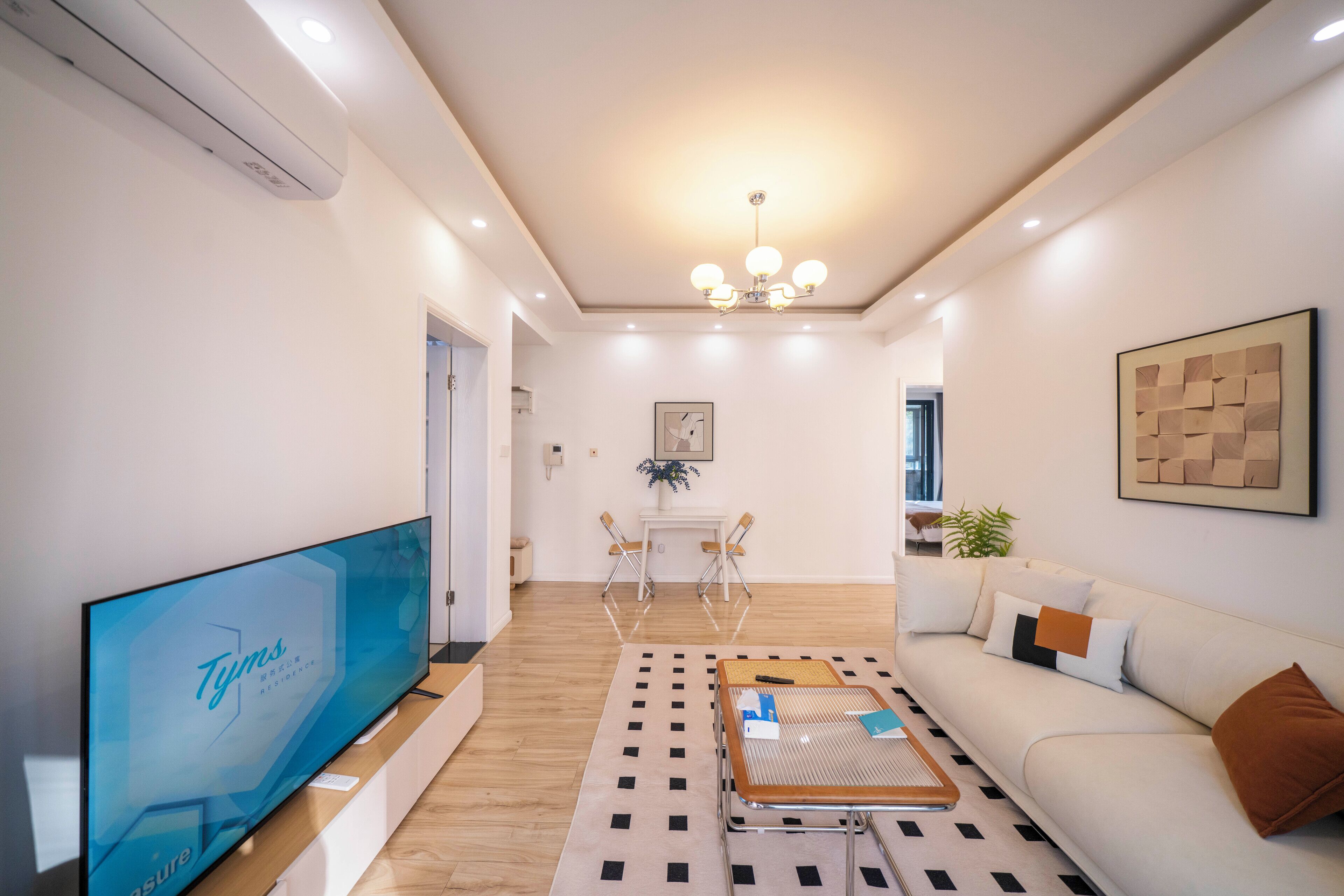 A modern living room with a flat-screen TV, a sofa, a coffee table, and a dining area with chairs and a small table.
