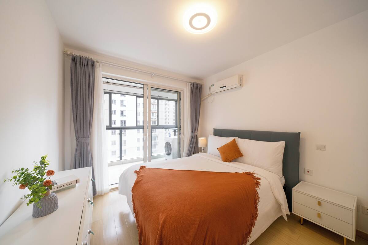 Una habitación de hotel moderna con una cama grande, una mesita de noche y un ventanal con cortinas.
