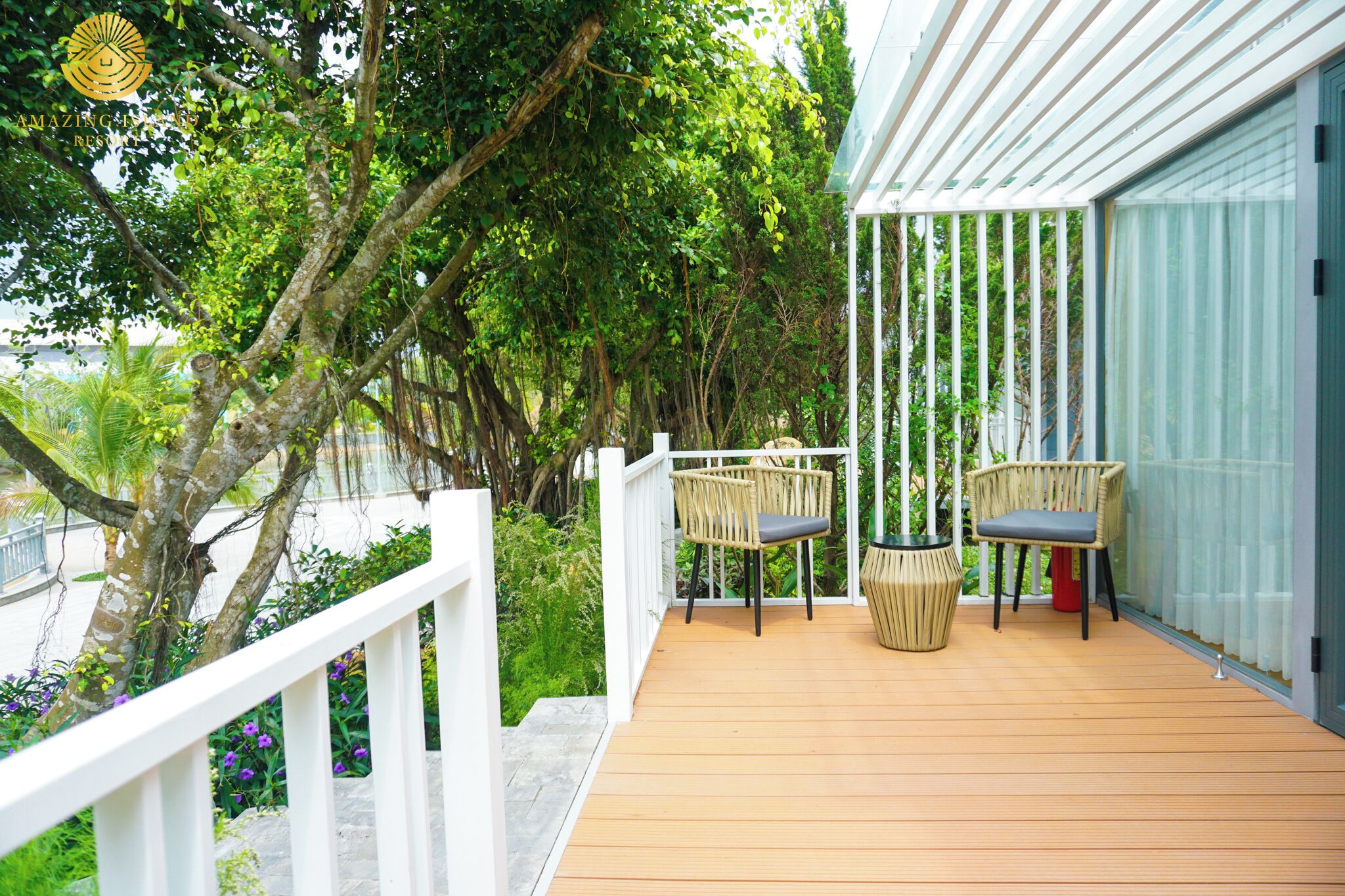 A wooden deck with two wicker chairs and a potted plant, surrounded by lush greenery and a white railing.