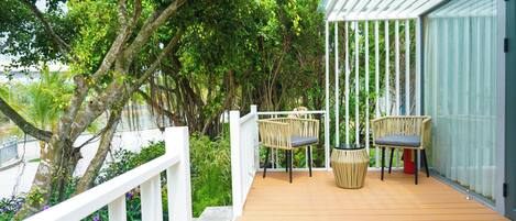 A wooden deck with two wicker chairs and a potted plant, surrounded by lush greenery and a white railing.