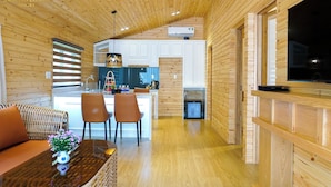 A wooden interior with a kitchen and dining area, featuring a sofa, chairs, and a TV. - Amazing Island Resort (Long Hung)