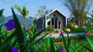 A resort with modern architecture, featuring a prominent entrance with glass doors, surrounded by lush greenery and tropical plants. - Amazing Island Resort (Long Hung)
