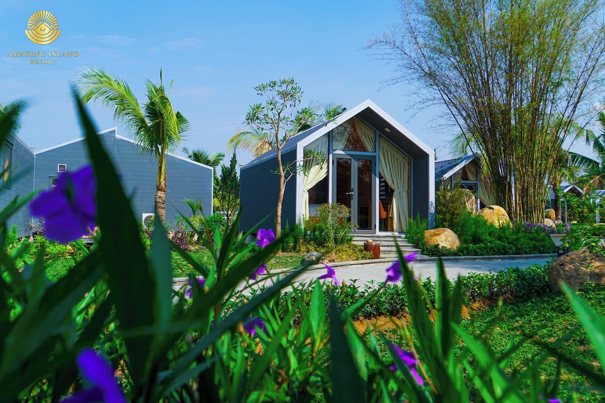 Resort com arquitetura moderna, apresentando uma entrada imponente com portas de vidro, cercado por vegetação exuberante e plantas tropicais.
