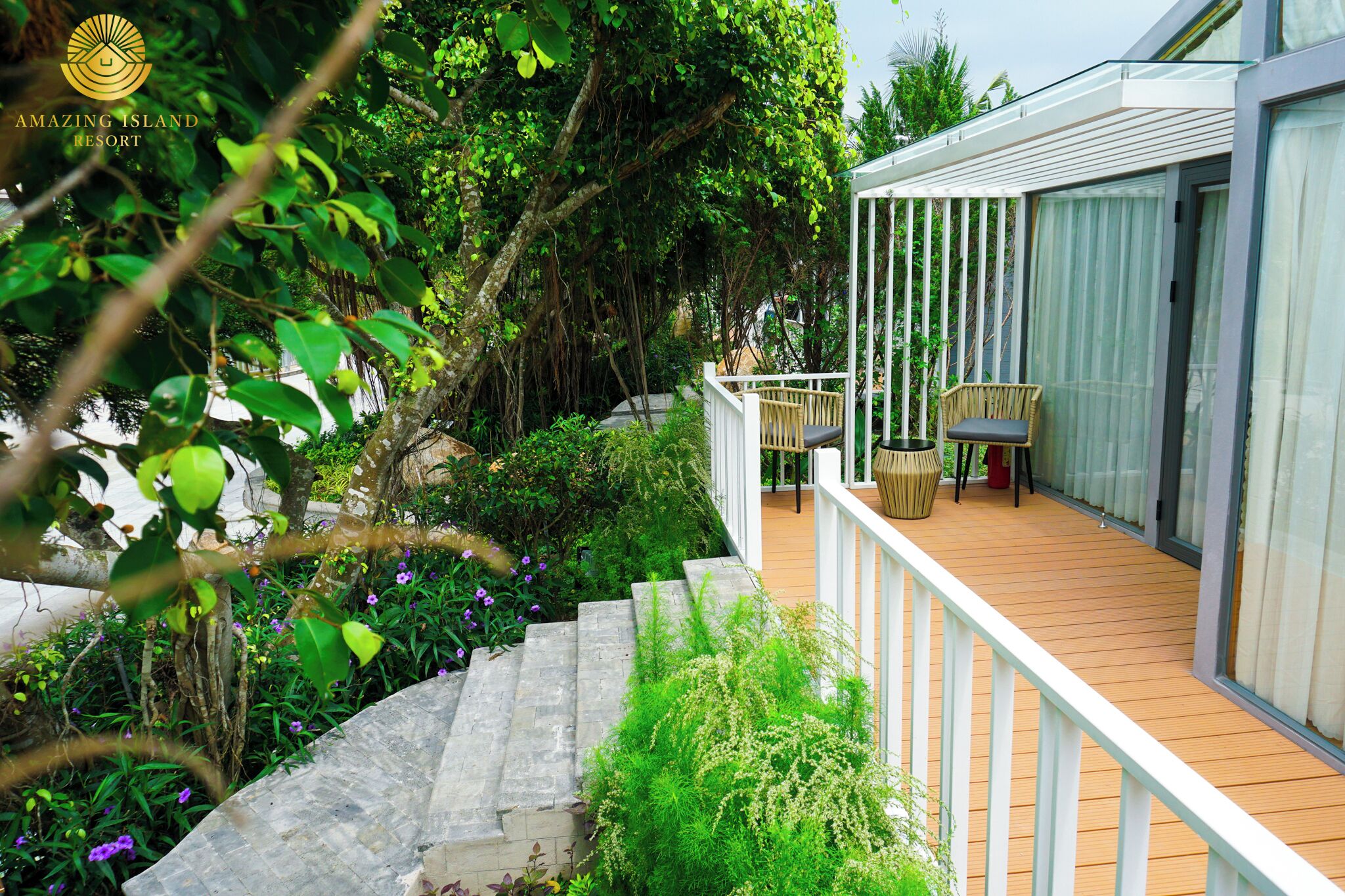 A wooden deck with a white railing, surrounded by lush greenery and a stone staircase.