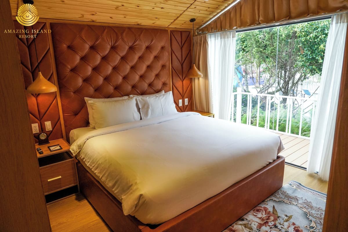 Quarto espaçoso com cama grande, cabeceira de madeira e varanda com vista para o verde.