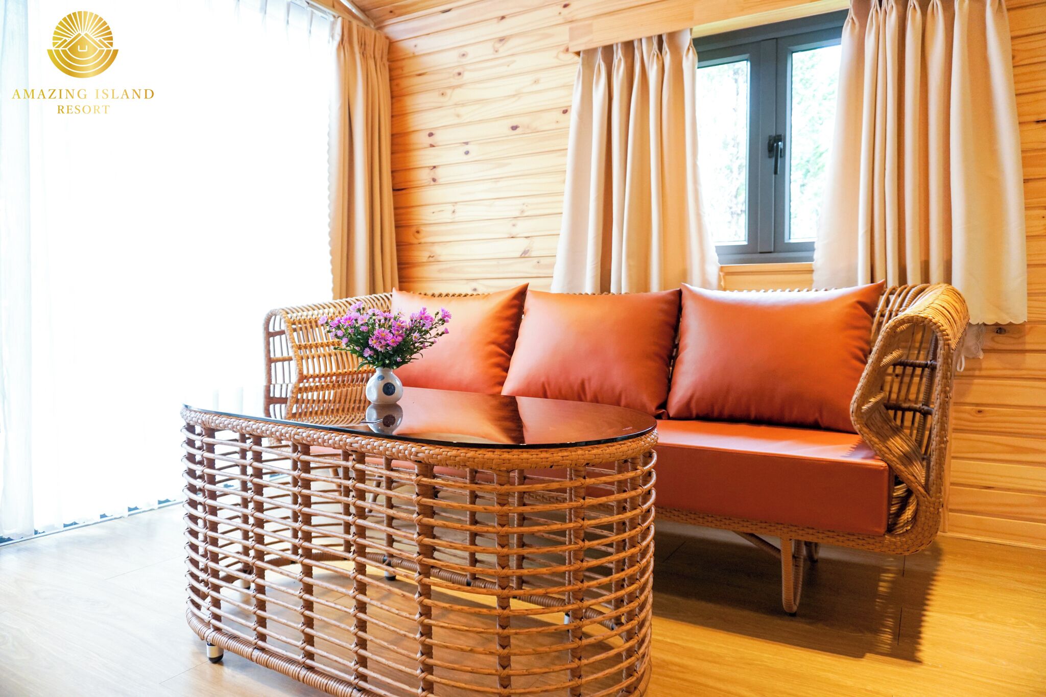 A cozy room with a wicker sofa and a round table, a window with curtains, and wooden walls.