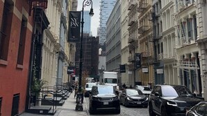 Una calle estrecha flanqueada por edificios históricos, con un rascacielos moderno al fondo y automóviles estacionados.