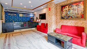 Un'area di accoglienza con parete decorata a motivi blu, una scrivania della reception, posti a sedere rossi e un grande quadro incorniciato.